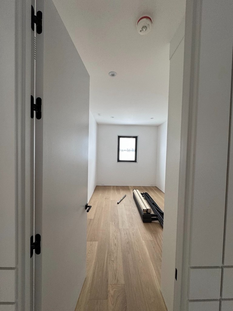 Bright empty room with white walls, light hardwood floors, and black door hardware.
